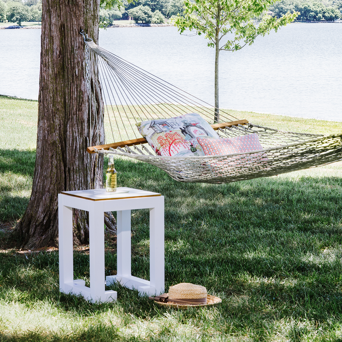 white end table from the Jamie Merida Collection outside by a hammock by the water
